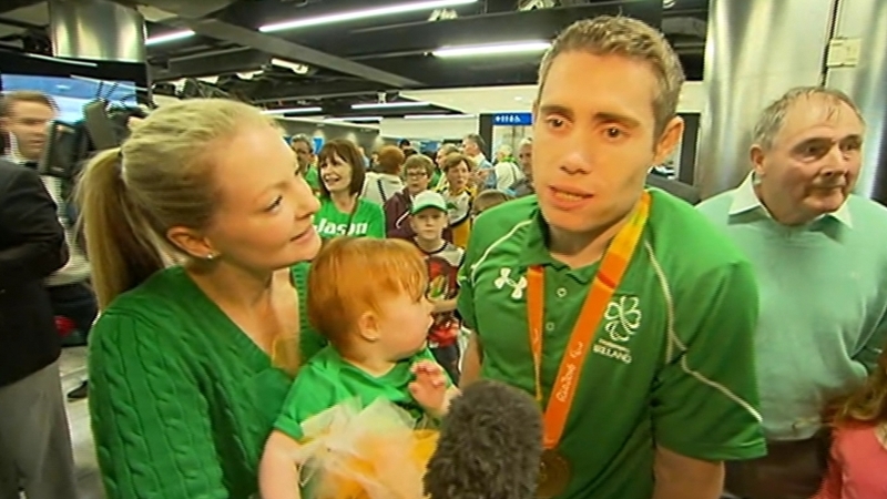 Gold medalist Jason Smyth is welcomed home by his wife and child