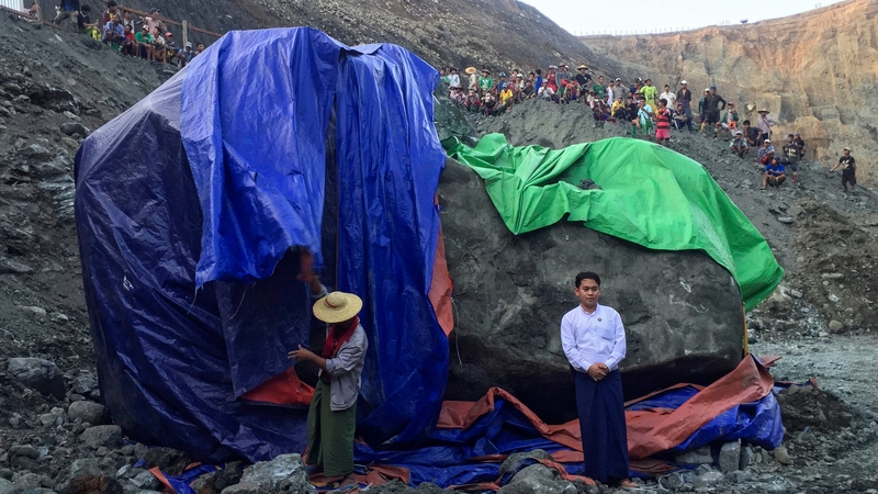 A man poses for photographs next to a worker preparing to cover the giant jade stone