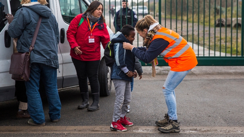A care worker brings a child to a reception point outside the 'jungle'
