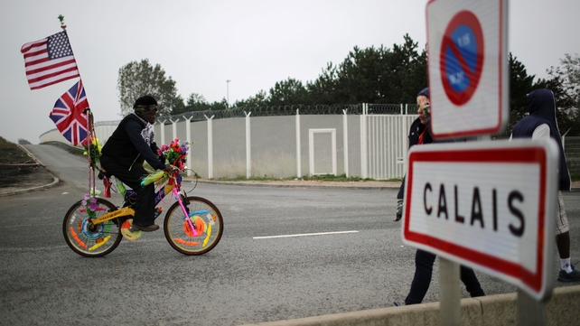 A migrant cycles on a bike with flowers and flags as migrants begin to leave the camp before authorities demolish the site