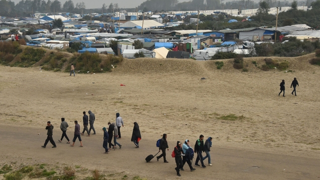 Migrants with their luggage leave the camp, as part of the evacuation operation