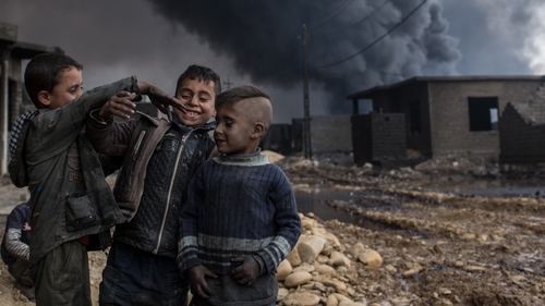 A group of boys play in a street outside their home in front of a burning oil well set on fire by fleeing IS members south of Mosul