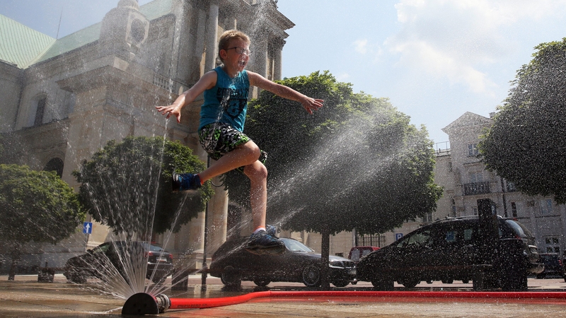 A child plays with water from a hose as they cool off on a hot day in Warsaw, Poland