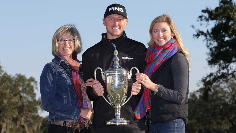 Mackenzie Hughes poses with the trophy alongside his wife and mother