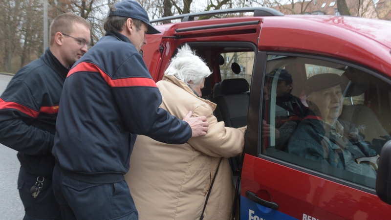 An elderly woman is helped by rescue workers