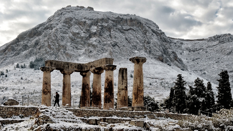 A person walks by the snow-covered temple of Apollo in Ancient Corinth, Greece