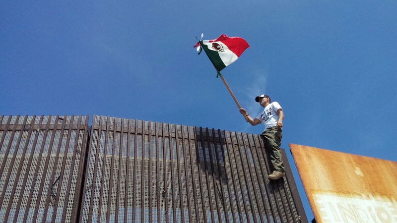 A US protester waves a Mexican flag at a border wall that divides Mexico and the US in Tijuana