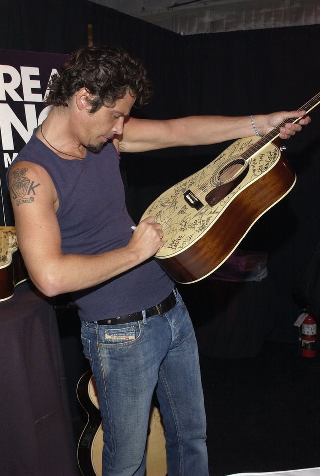 The charitable Chris shows off a shoulder tattoo as he signs a Gibson guitar to be auctioned off while backstage at the 'ReAct Now Music & Relief' benefit concert in 2010.
