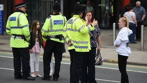 A young girl wearing a t-shirt of US singer Ariana Grande stands with women talking to police near Manchester Arena