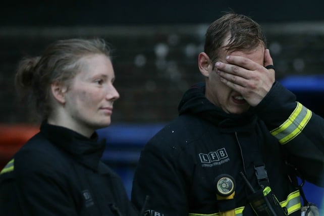 Fire fighters react as the Grenfell tower burns on