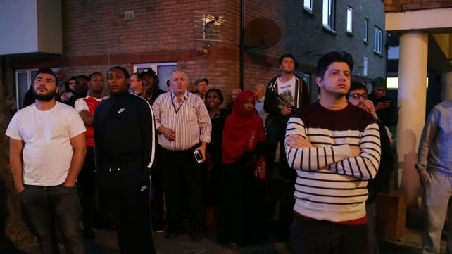 Local residents look on as the 24-storey residential tower is engulfed in flames