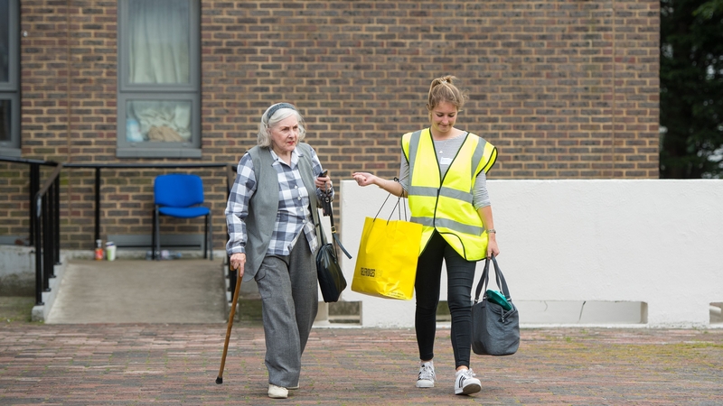 A council worker helps a resident leaving the Dorney tower on the Chalcots Estate, in London