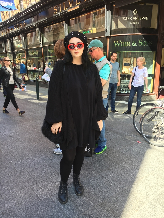 Mary Keane wears a cardigan from Urban Outfitters over a dress from Mango. Her beanie is from Bio Hazard and her glasses are from Cobra Snake. She is wearing vegan Dr. Martens boots.