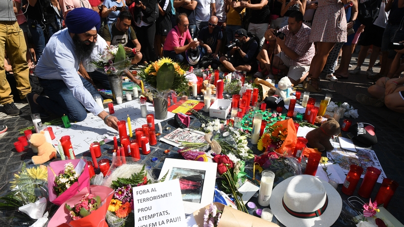 People stand next to flowers, candles and other items set up on the Las Ramblas boulevard as they pay tribute to the victims