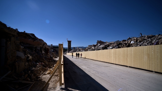 People walk through the remains of Amatrice one year one