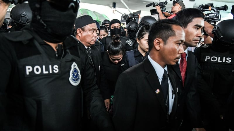 One of the two women charged is escorted through the airport