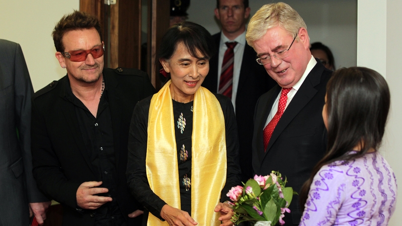 Aung San Suu Kyi and Bono meet Eamon Gilmore as she is presented with flowers upon her arrival at Dublin Airport in 2012