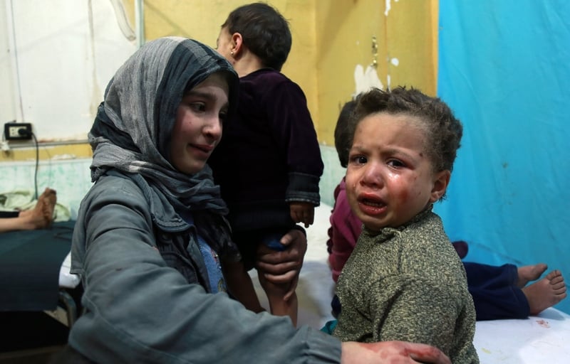 A Syrian girl looks at another crying child sitting on a hospital bed in a make-shift clinic in the besieged Eastern Ghouta region today