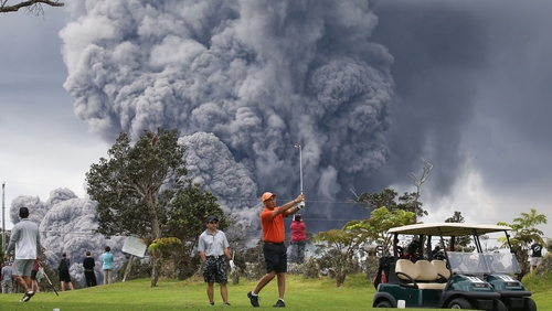 People play golf as an ash plume rises in the distance from the Kilauea volcano on Hawaii's Big Island