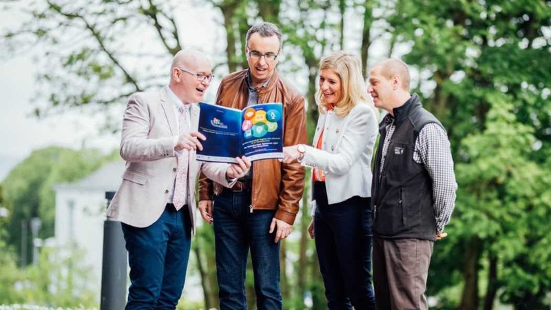 An Dr TJ Ó Ceallaigh, (clé) stiúrthóir na comhdhála ar an dTumoideachas ag míniú cuid den clár do thoscairí eile