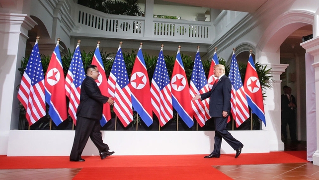 In this handout photo, Kim Jong-un (L) and US President Donald Trump approach each other for their first meeting