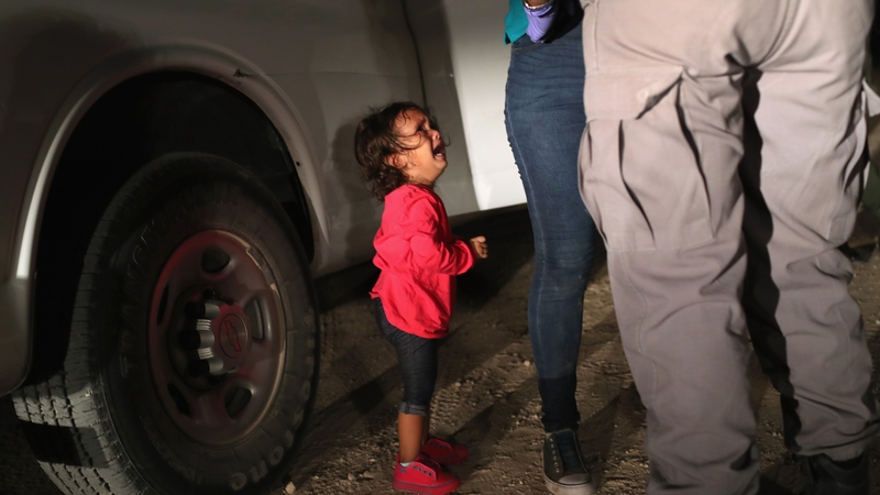A two-year-old Honduran girl cries as her mother is searched and detained near the US-Mexico border