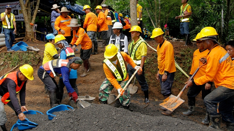 Thai workers transport soil to adjust the ground in front of the Tham Luang cave