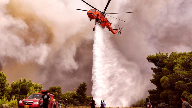 Firefighters and volunteers try to extinguish flames during a wildfire at the village of Kineta, near Athens