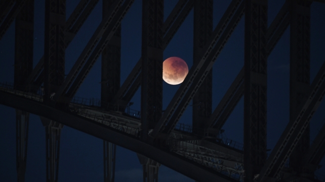 The moon is seen behind the Harbour Bridge in Sydney