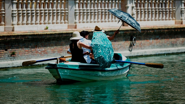 People protect themselves from the sun with umbrellas while they take a boat ride at Parque de Maria Luisa, in Seville, Spain