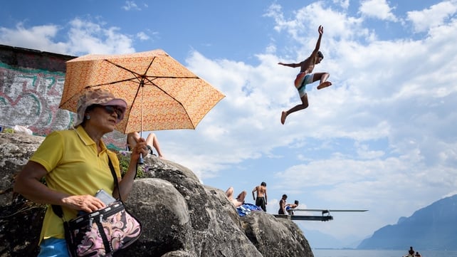 A boy jumps into Geneva Lake in Saint Saphorin, Switzerland, as a tourist protects herself from the sun with an umbrella