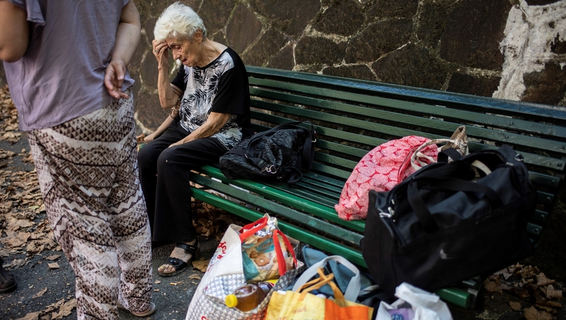 An elderly woman sits on a bench after she was evacuated from her apartment