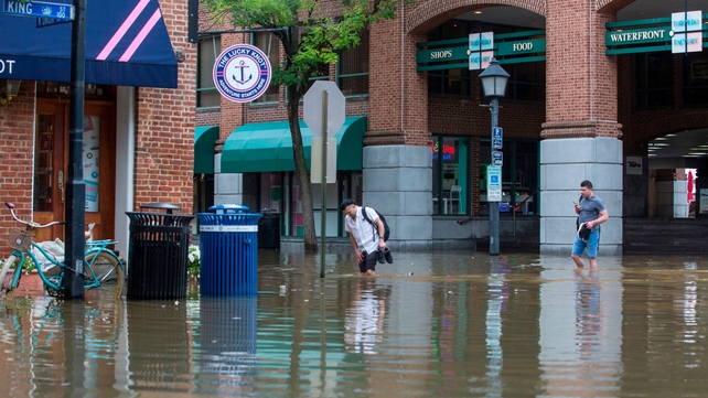 People cross the street as water floods from rain outside buildings in Old Town Alexandria, Virginia