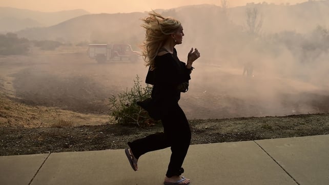A woman runs as firefighters work to control a flare up due to flying embers from the Woolsey Fire in Calabasas