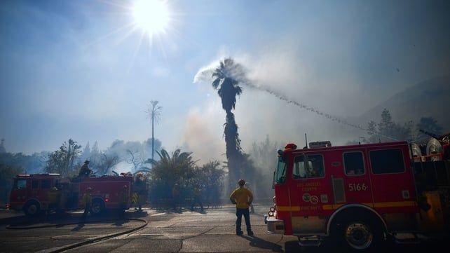 Firefighters water down trees and bushes near homes on Bell Canyon Road in West Hills