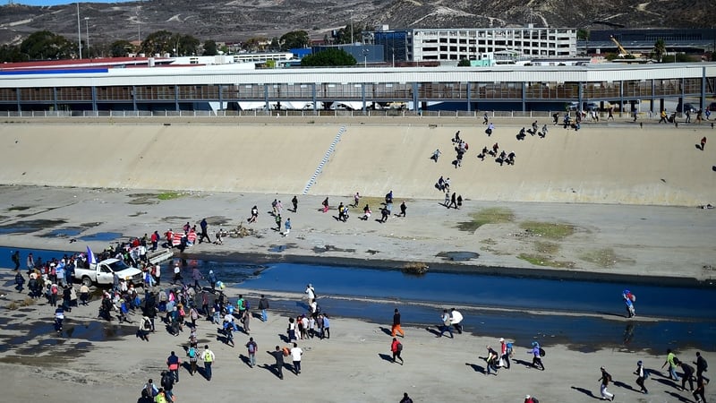 Migrants cross the dry riverbed of the Tijuana River trying to get to the El Chaparral port of entry