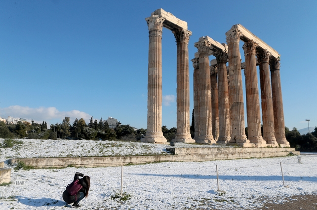 A young girl takes pictures of the snowy Temple of Olympian Zeus in central Athens, Greece