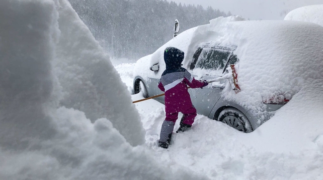 A boy clears a car window of snow in Salzburg, Austria as new snow falls