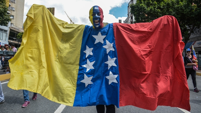 <p>A protester, his face painted with the Venezuelan flag colours, wearing the country's flag</p>