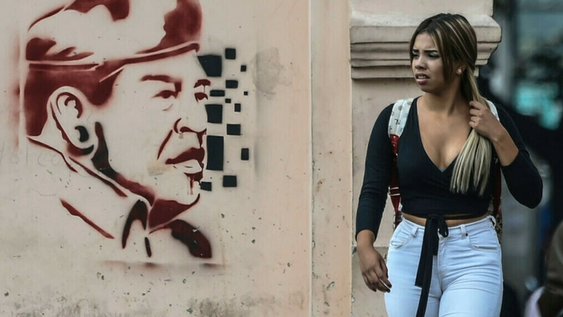 A woman walks past graffiti of late former Venezuelan president Hugo Chavez