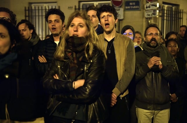 People react as they look at the firemen operations as the flames burn the roof of the Notre-Dame Cathedral in Paris