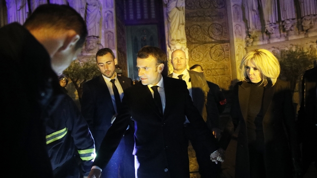 French President Emmanuel Macron (C) and his wife Brigitte Macron (R) pay a visit to firefighters at the scene