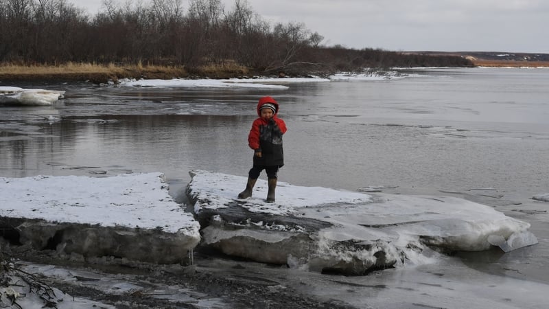 A child plays on melting ice beside severe erosion of the permafrost tundra at Yupik Eskimo village of Napakiak, Alaska