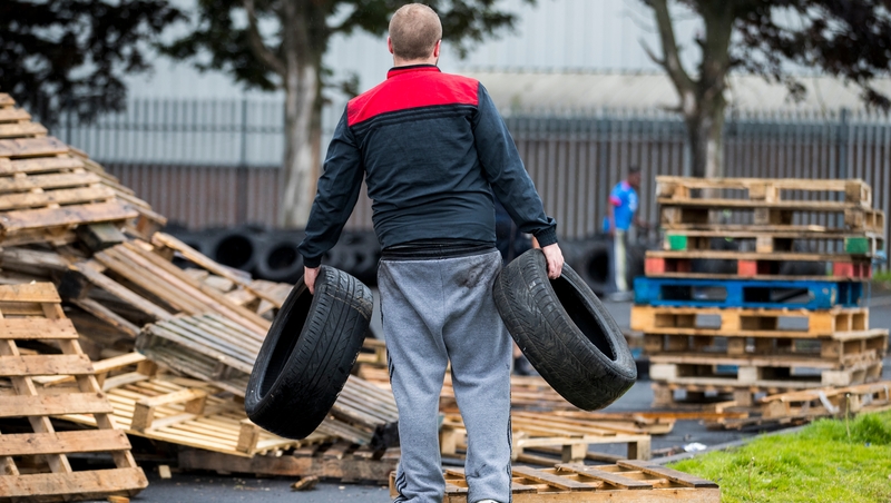 A man carries away tyres from the bonfire at the Avoniel Centre
