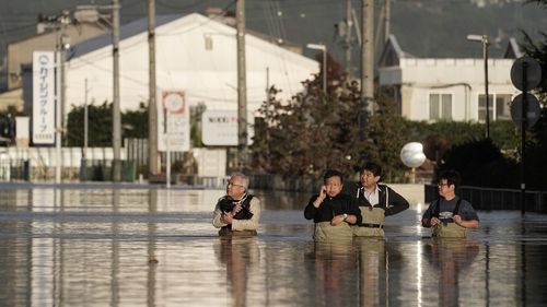 A group of men wearing chest-high waders check the condition of their office in a typhoon Hagibis flooded street in Nagano