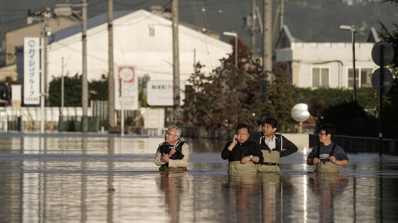 A group of men wearing chest-high waders check the condition of their office in a typhoon Hagibis flooded street in Nagano