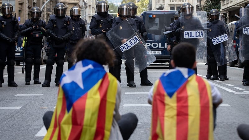Protesters wrapped up with Catalan pro-independence flags sit opposite riot policemen in Barcelona