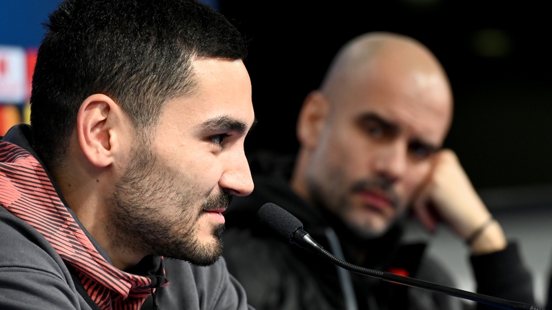 Manchester City head coach Pep Guardiola (R) looks on as Ilkay Gundogan speaks to the press