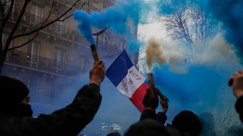 Protesters burn blue flares and wave a French flag during a demonstration in Paris