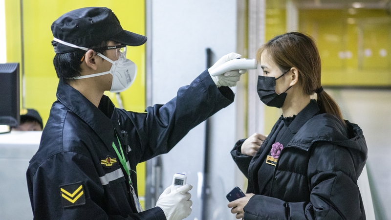 A security guard checks a passenger's body temperature at the entrance of a subway station in Guangzhou
